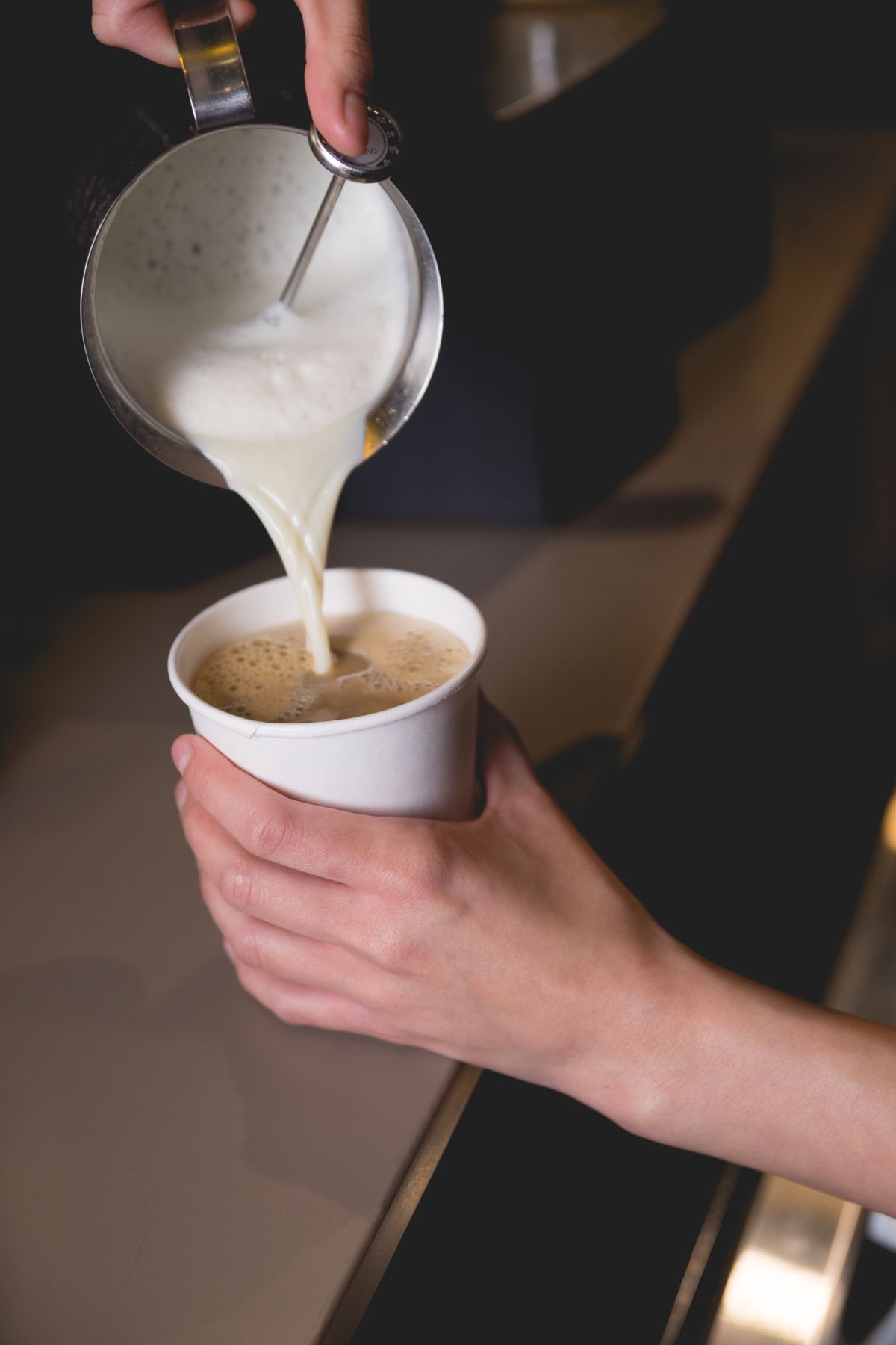 Female barista pours frothed milk into cup