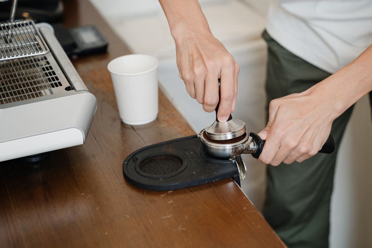 Crop barista grounding coffee in portafilter